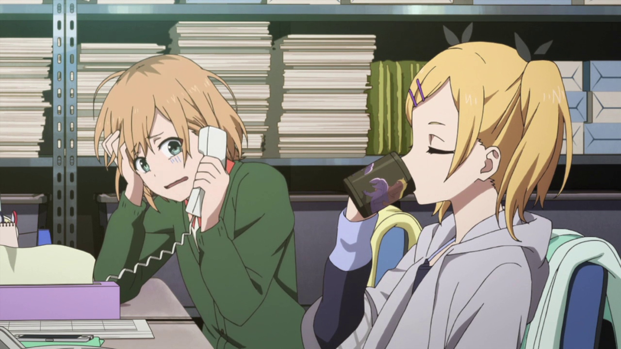 Miyamori and Yano from Shirobako at their desks. Miyamori is on the phone and freaking out while Yano is sipping coffee.