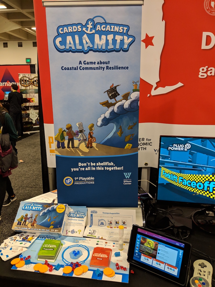 Table displaying physical cards for Cards Against Calamity and a video game version on a tablet.