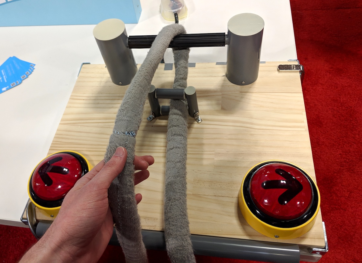 A hand holding a loop of gray rope tied to a roughly made controller with left and right buttons.