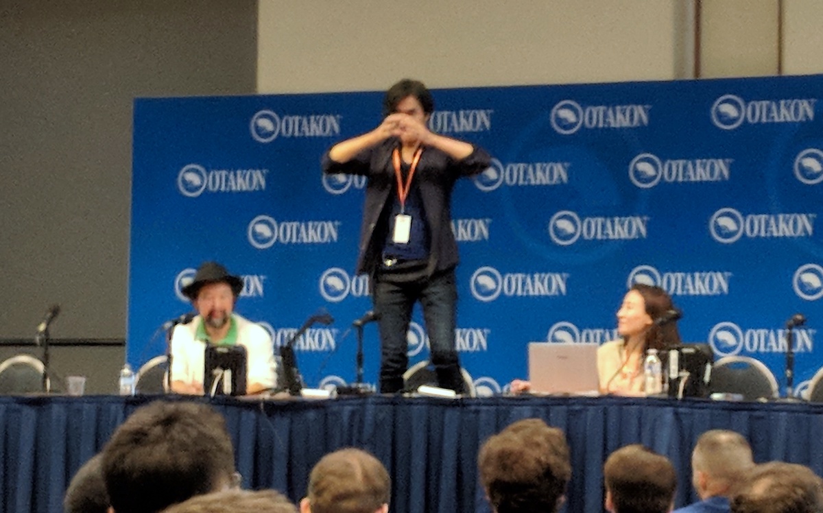 Shoji Kawamori standing up on the table at his panel