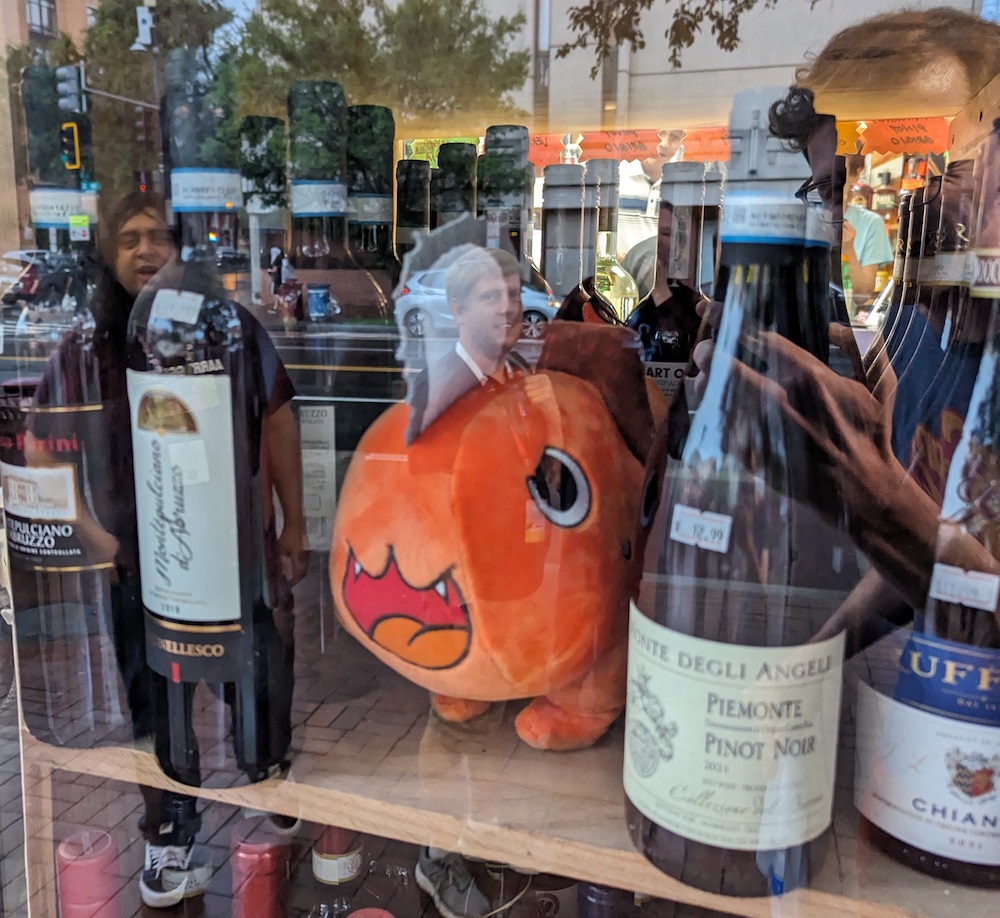 A Pochita plushie in between wine bottles at a storefront.
